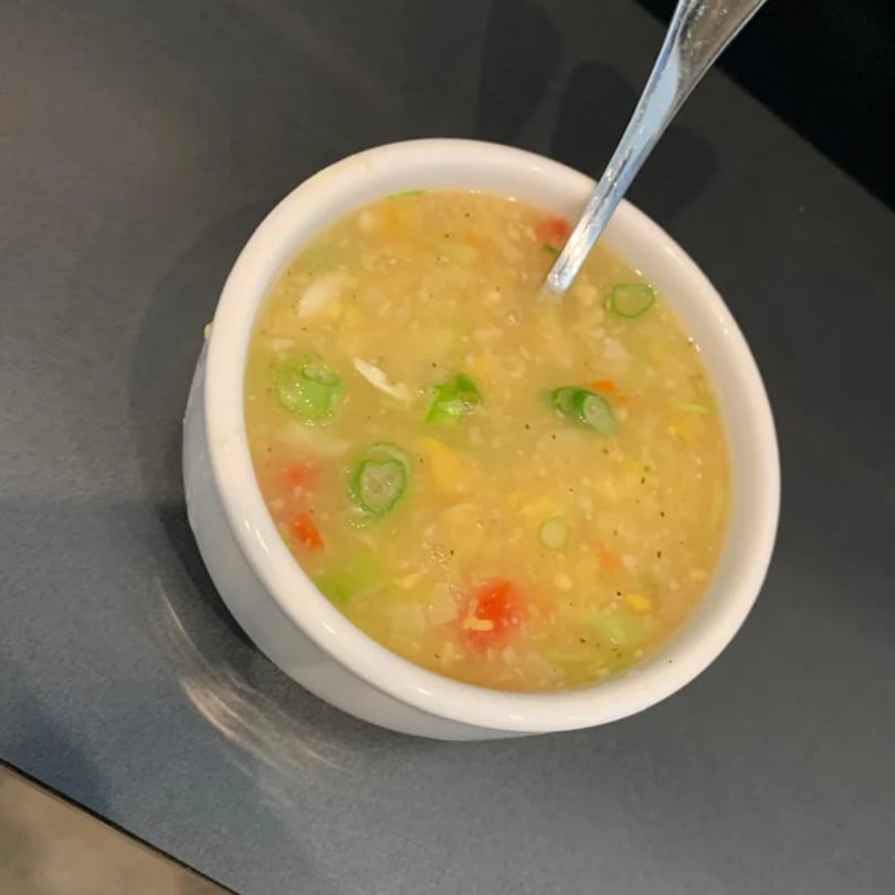 A white bowl of Indian vegetable soup with a spoon, garnished with green onions and red peppers.